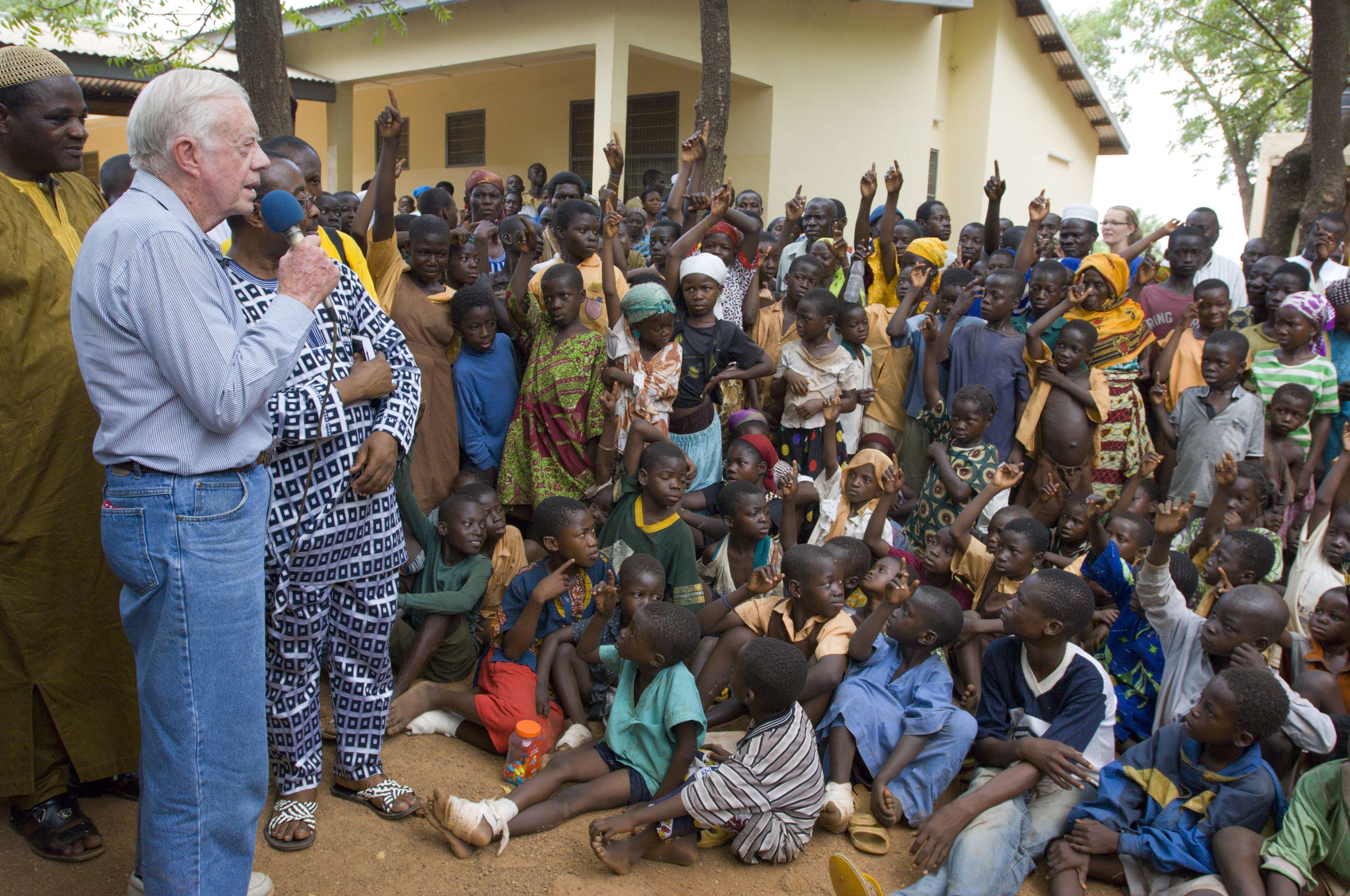 February 8, 2007. Savelugu Hospital, Northern Province, Ghana. President Jimmy Carter and his wife Rosalynn address Savelugu children on the seriousness of eradicating guinea worm disease. In this photo he has said "Hands up all those who have had Guinea Worm" and many of the children put up their hands.